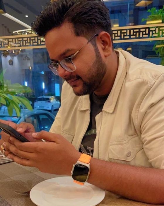 Aditya at a restaurant table, looking at his phone and smiling